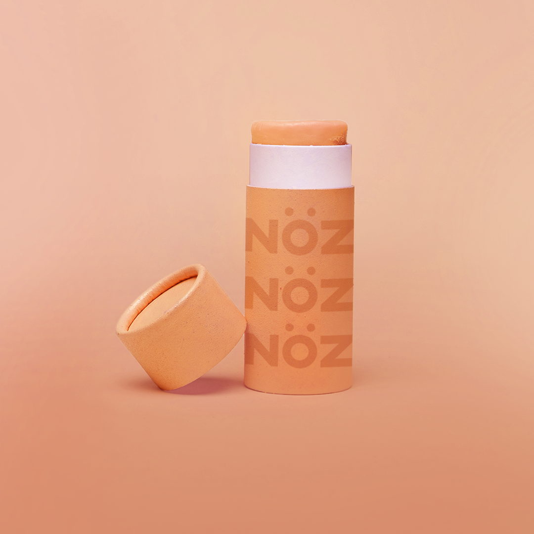 Close up of Nöz sunscreen in the color orange in earth friendly container with the lid off